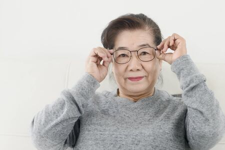 Happy Asian senior woman wearing eyeglasses and sitting on sofa at home, lifestyle concept.の写真素材