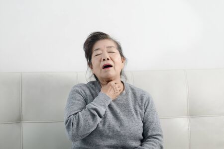 Asian senior woman have a cough while sitting on sofa, lifestyle concept.の写真素材