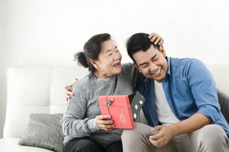 Happy Asian man giving gift box to his mother for Mother's Day celebration.の写真素材