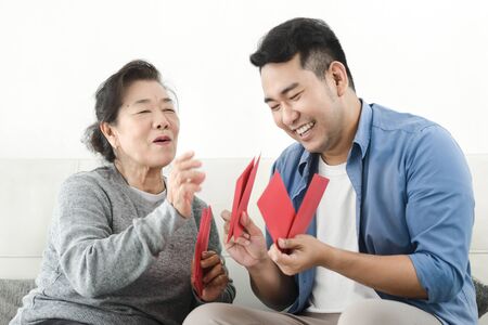 Happy Asian mother give red envelopes containing cash to her son for Chinese New Year concept.