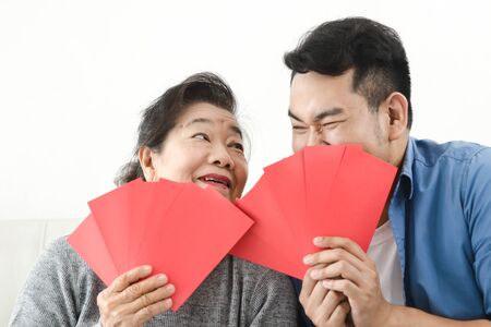 Happy Asian mother give red envelopes containing cash to her son for Chinese New Year concept.