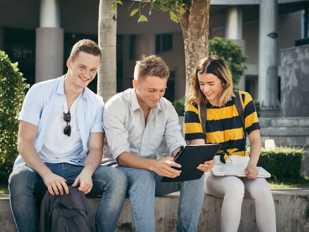 Happy university student using tablet together outside building with natural light.