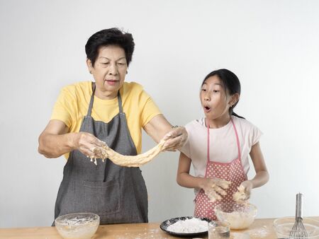 Asian senior woman and girl making dough for homemade pizza or bread, lifestyle concept.の写真素材