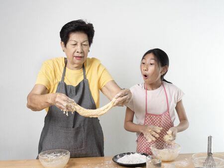 Asian senior woman and girl making dough for homemade pizza or bread, lifestyle concept.