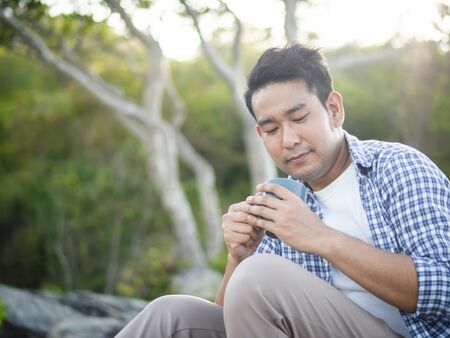 Asian man holding coffee cup with nature outdoor, lifestyle concept.