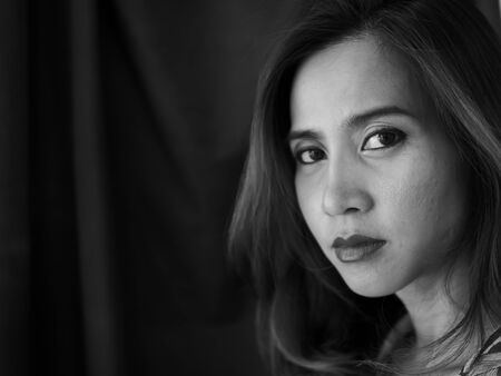 Asian woman looking out window, black and white.の写真素材