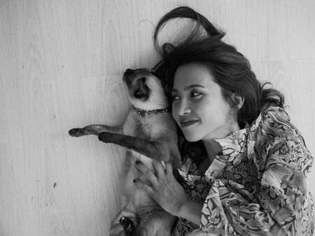 Asian woman lying on floor while playing with her cat, black and white.の写真素材
