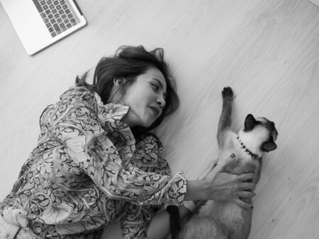 Asian woman lying on floor while playing with her cat, black and white.の写真素材