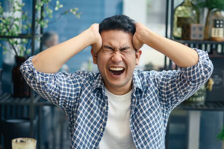 Depressed Asian man using smartphone in cafe, lifetyle concept