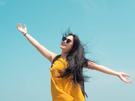 Asian woman with backpack raising hands with blue sky.の写真素材