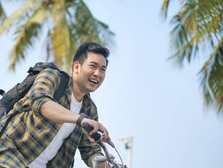 Happy Asian man with backpack riding bicycle with green tree