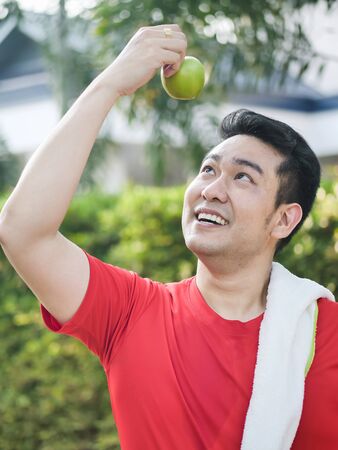 Happy Asian sport man with green apple in his hand outdoor.の写真素材