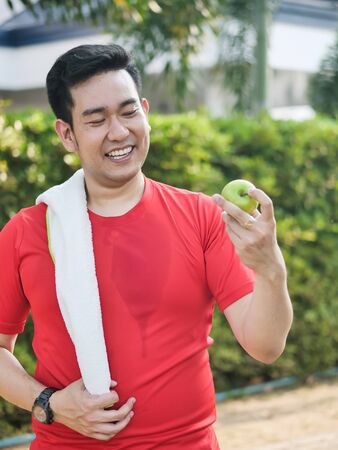 Happy Asian sport man with green apple in his hand outdoor.の写真素材