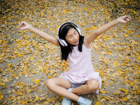 Asian girl wearing headphone and sitting on yellow leafs outdoor, lifestyle concept.の写真素材