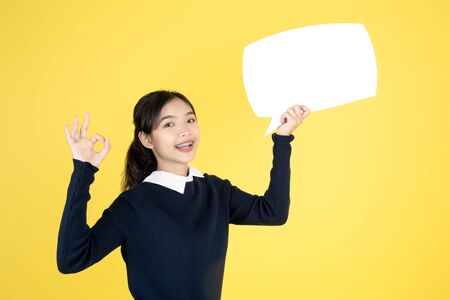 Asian teeanger holding white speech bubble on yellow background.の写真素材