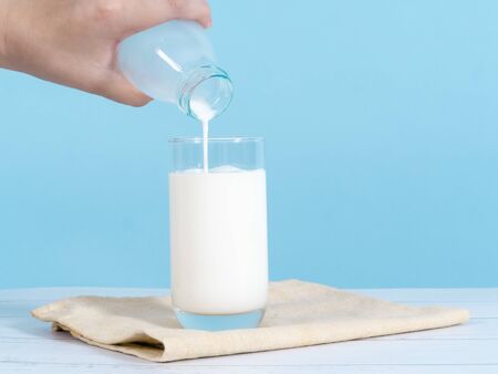 Kid hand pouring milk into glass with blue background.の写真素材