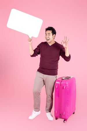 Happy Asian tourist holding speech bubble with luggage on pink background.の写真素材