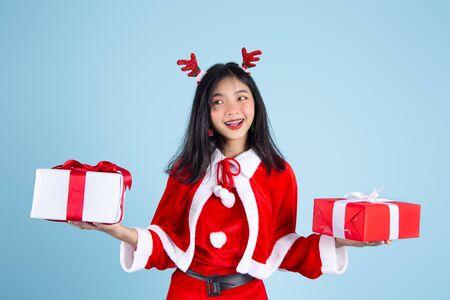 Happy Asian in Santa Claus costume holding Christmas  gift box on blue background.の写真素材