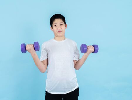 Smiling Asian boy using dumbbell on blue background.の写真素材