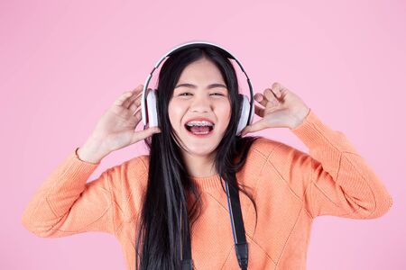 Happy Asian girl in orange sweater using headphone on pink background.の写真素材