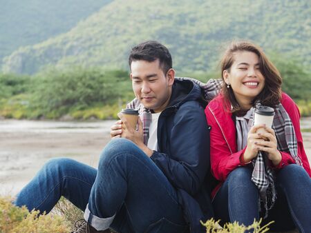 Happy Asian couple camping and drinking coffee with nature background, lifestyle concept.