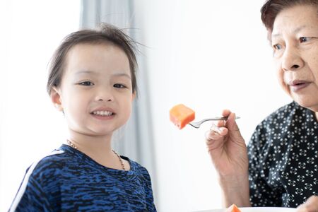 Grandmother feeding her child with ripe papaya sliced.