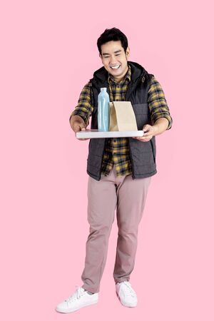 Delivery man is carrying lunch box and drink takeaway to customer on pink background.の写真素材