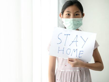 Asisan girl wearing mask holding paper message STAY HOME, during COVID-19.の写真素材
