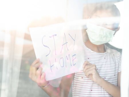 Asisan girl wearing mask holding paper message STAY HOME, during COVID-19.の写真素材