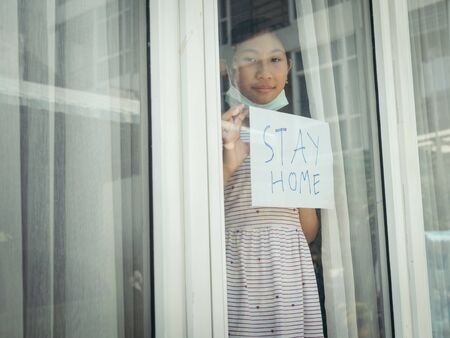 Asisan girl wearing mask holding paper message STAY HOME, during COVID-19.の写真素材