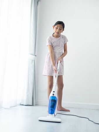 Asian girl using vacuum cleaner, girl standing near window at home during COVID-19.の写真素材