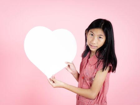 Asian preteen girl holding white heart shape speech bubble on pink background.の写真素材