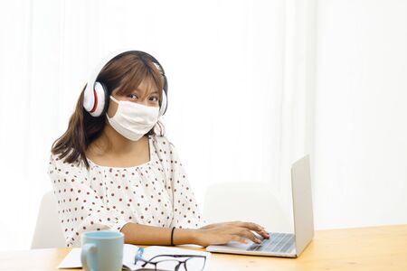 Asian teenager girl wearing mask using laptop for home schooling online  and quarantine concept.