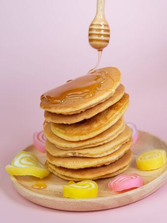 Pouring honey syrub on pancake stack on pink background.の写真素材
