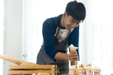 Asian teenager boy decorating cupcakes at home, lifestyle concept.の写真素材