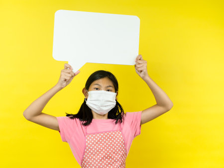 Asian girl showing blank speech bubble on yellow background.の写真素材