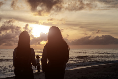 silhouettes two teenage girls  tourists waiting to see sunrise from the seaの写真素材