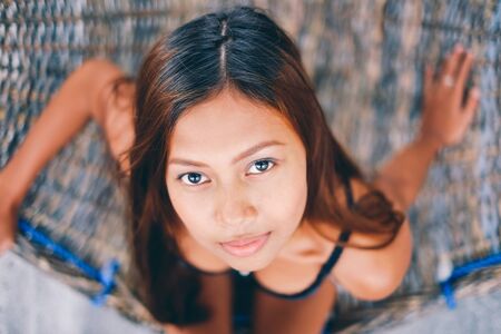 Portrait of young sexy beautiful girl sitting on rattran hammock on the beach during the summerの写真素材