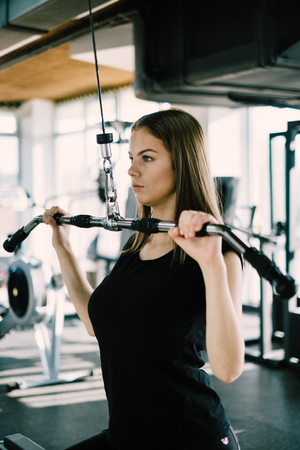 Young beautiful girl exercising in the fitness gym, with lat machine