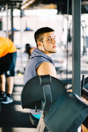 Attractive muscular bodybuilder taking rest from exercises with barbell in a gym. Guy bodybuilder...