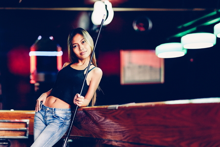 Young beautiful girl in a billiard club, with cue stick posingの写真素材