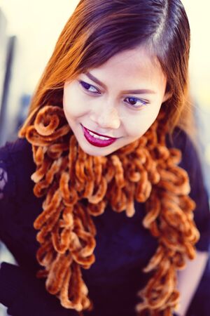 Young beautiful girl in black dress with brown scarf sitting on the benchの写真素材