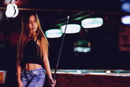 Young beautiful girl in a billiard club, with cue stick posingの写真素材