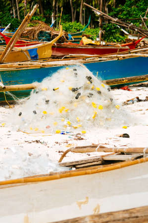 White fishing net on coral sand beach with colorful boats and palms in backgroundの写真素材