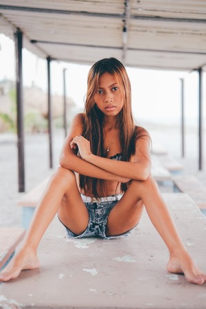 Beautiful girl sitting on the concrete table beneath the sunshadeの写真素材