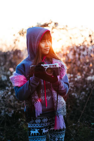 Young beautiful girl holding camera outside during the sunset