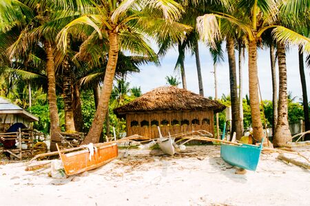 Native nipa hut with small fishing boats in front on beautiful white sand beachの写真素材