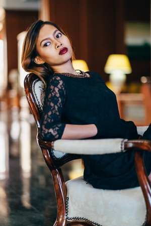 Elegant young beautiful woman in gorgeous silk dress sitting in antique armchairの写真素材