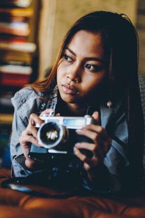 Beautiful girl with a vintage retro film camera lying on leather sofaの写真素材