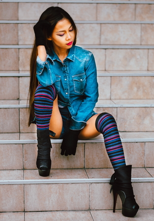 Fashionable pretty young woman wearing striped knee socks sitting on the stairsの写真素材